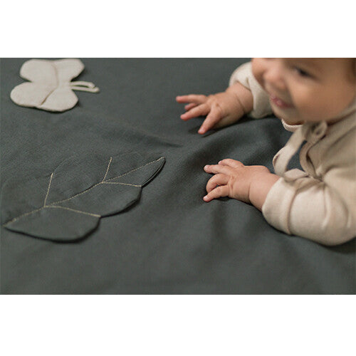 Een baby speelt met een stoffen blad op het donkergroene babyspeelkleed.