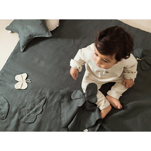 Een baby zit op het donkergroene babyspeelkleed met stoffen bladeren en vlinders.
