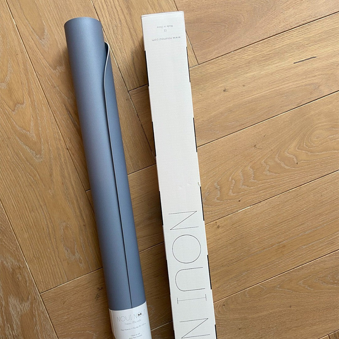 Een opgerolde dusty blauwe noui noui knoeimat ligt naast de witte verpakking op een houten vloer.