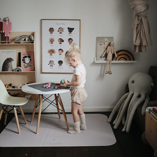 Een kind speelt aan een tafel, staand op een lichtgrijze noui noui knoeimat in een kinderkamer.