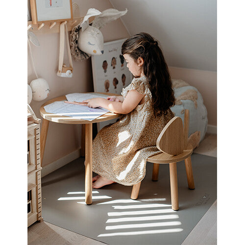 Kind zit aan een houten tafel met de Noui Noui knoeimat op de vloer.