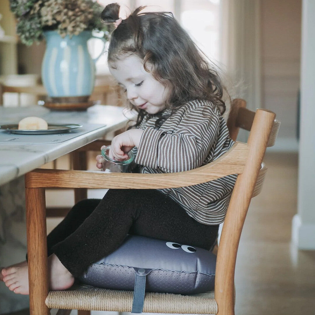 Een kind zit op het noui noui opblaasbare stoelkussen in een houten kinderstoel aan tafel.