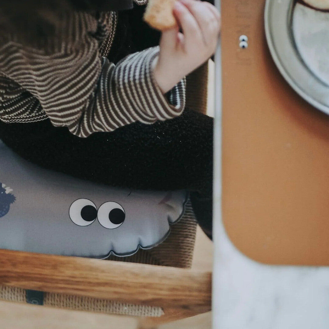 Een kind zit op het noui noui opblaasbare stoelkussen met dinosaurusogen in een houten kinderstoel.