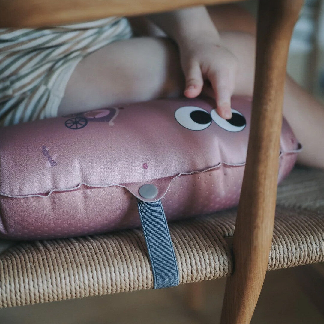 Een kinderhand raakt de ogen van het roze opblaasbare stoelkussen op een houten stoel.