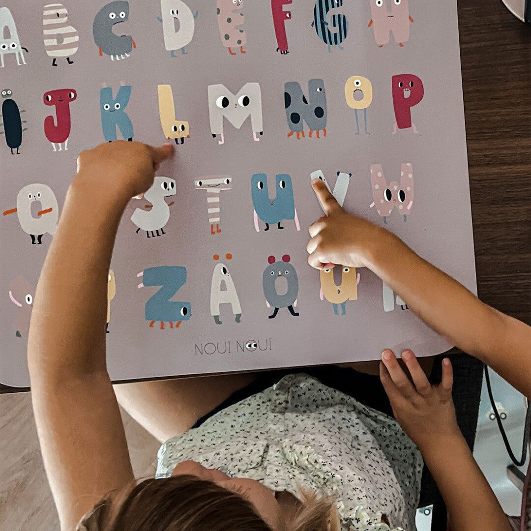 Twee kinderhanden wijzen naar letters op de Noui Noui ABC placemat.
