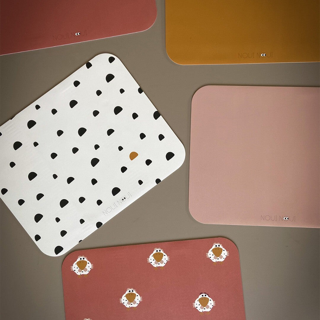 Een collectie noui noui placemats in verschillende kleuren en patronen, waaronder wit met zwarte stippen en roodbruin met schaapjes.