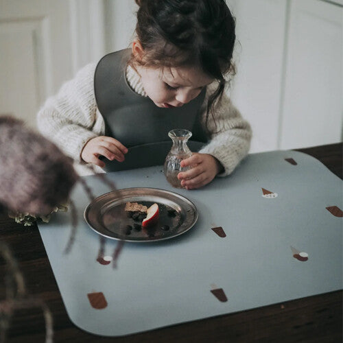 Een kind zit aan tafel met een Noui Noui grijze placemat met ijsjespatroon en een bordje met eten.