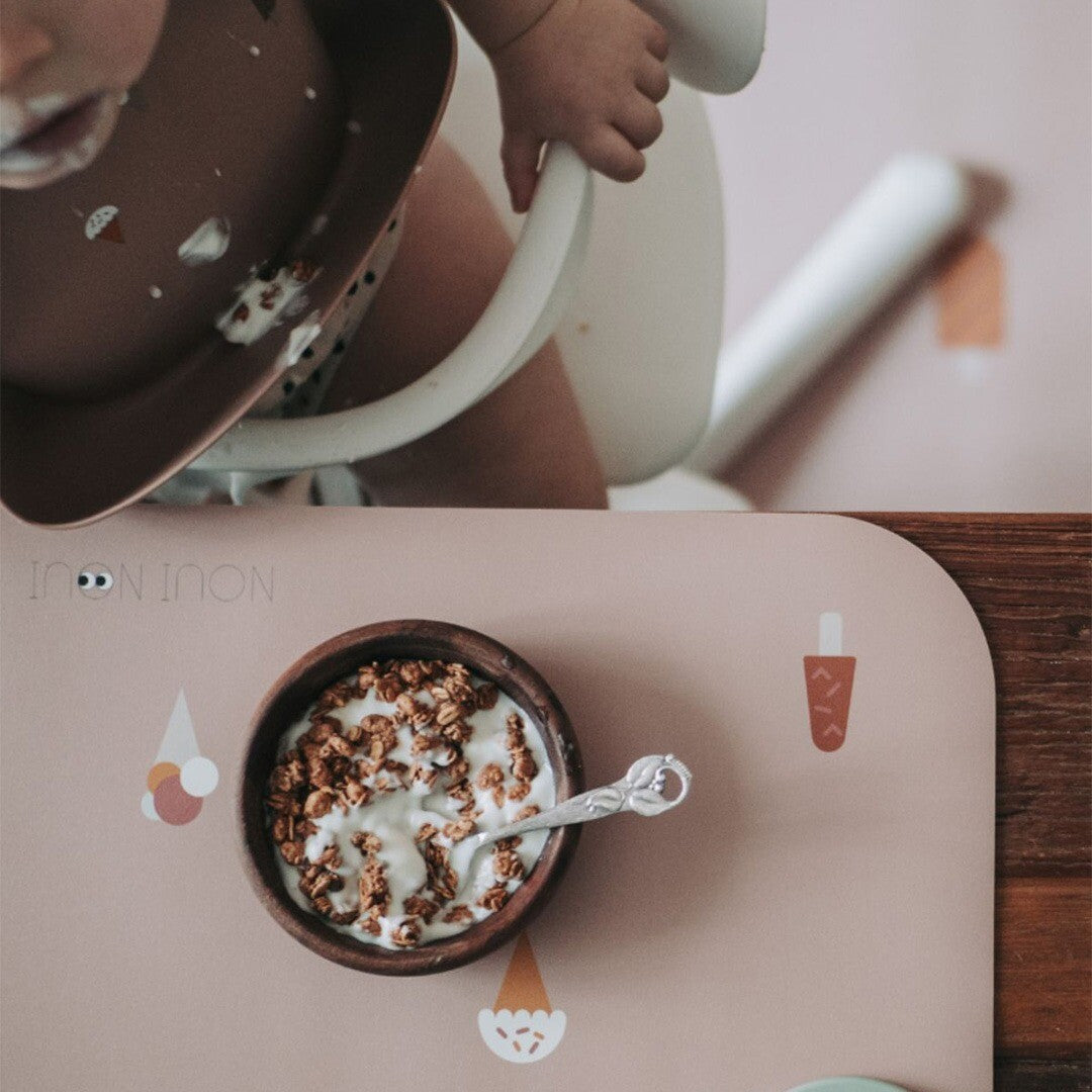 Een baby eet uit een kommetje op een roze Noui Noui placemat met ijsjespatroon.