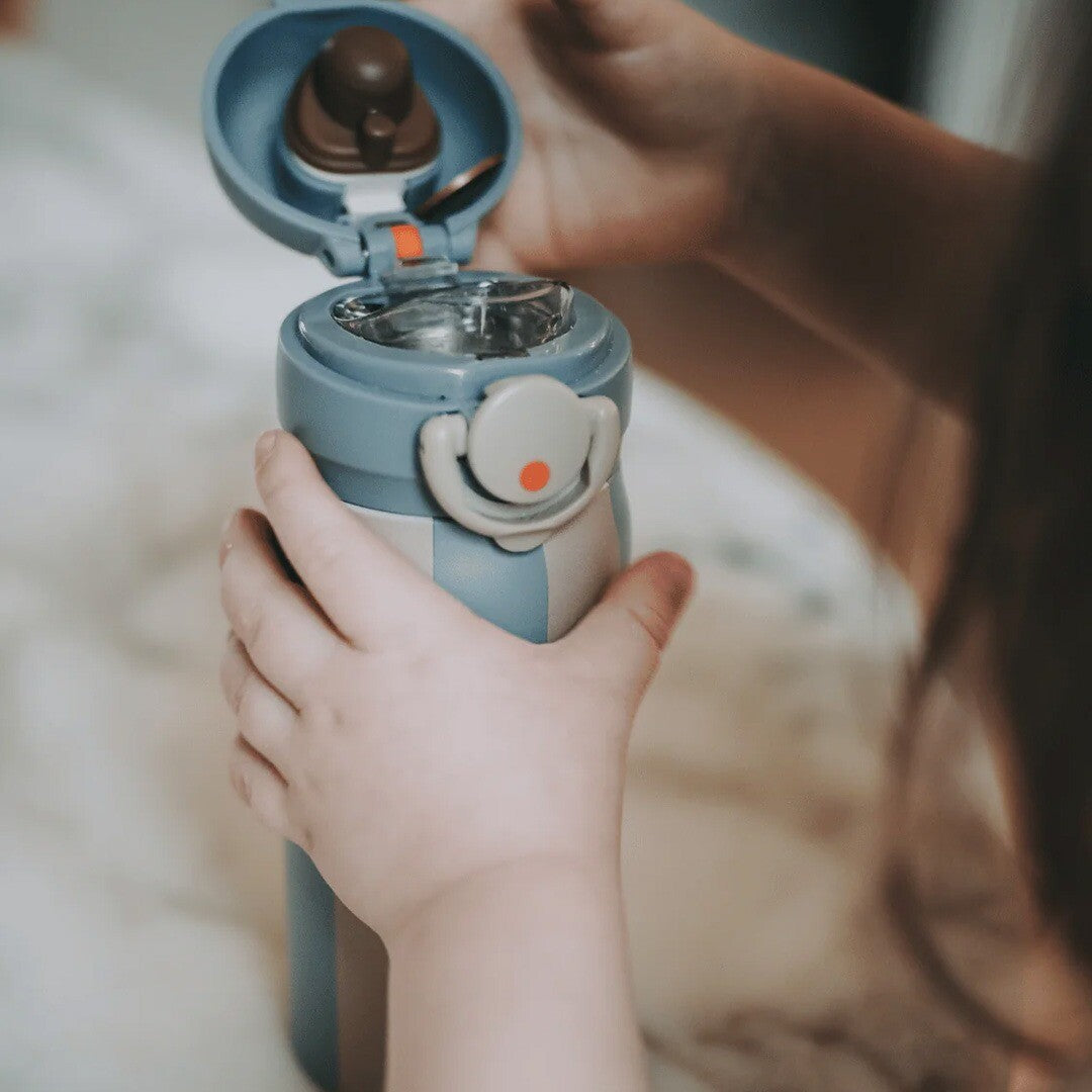 Kinderhandjes houden de noui noui thermosfles met dino-opdruk vast, met de dop open.