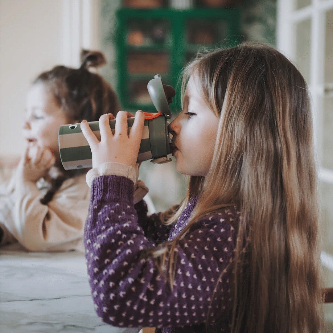 Een meisje drinkt uit de noui noui kinderthermosfles met krokodil en strepen.
