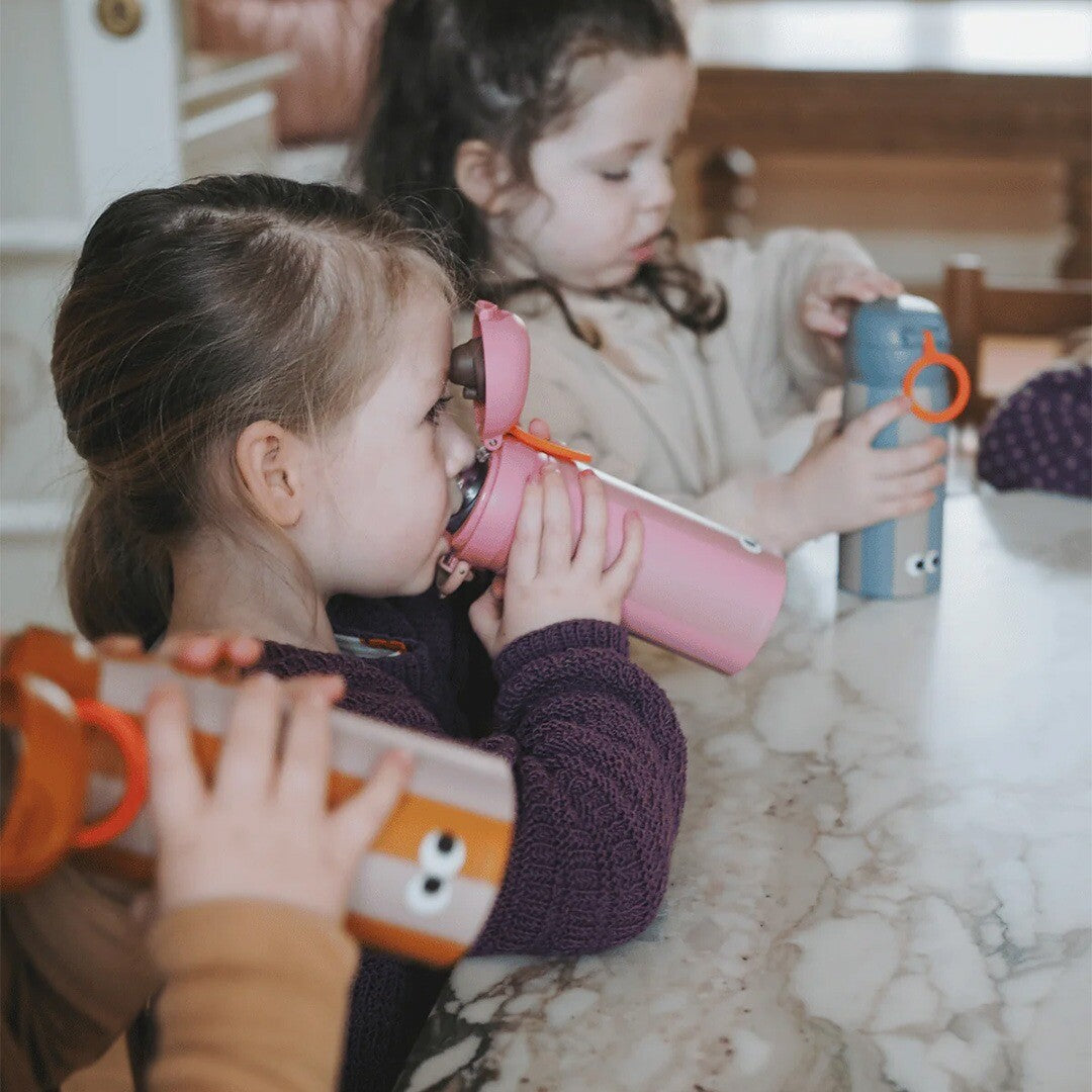 Twee kinderen drinken uit en spelen met verschillende gekleurde thermosflessen.