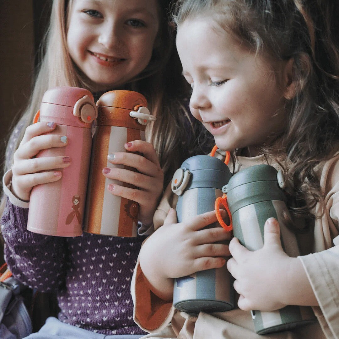 Twee lachende meisjes houden een collectie van vier noui noui rvs thermosflessen vast.