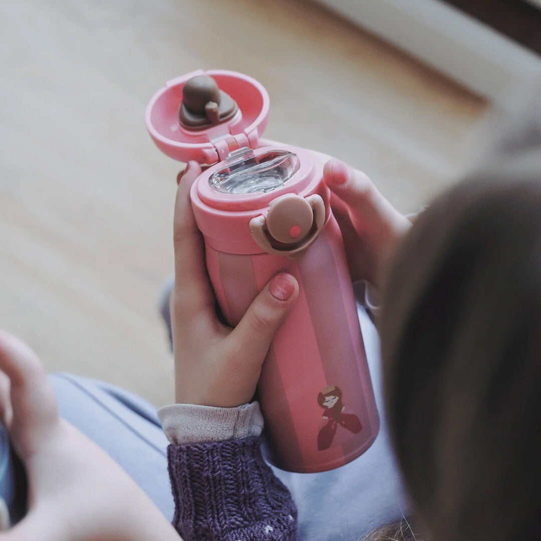 Kinderhanden houden een open roze gestreepte noui noui rvs thermosfles met prinsesfiguur vast.