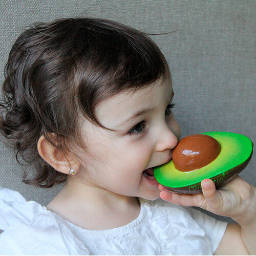 Een peuter bijt op het oli & carol bijtspeelgoed in de vorm van een avocado.