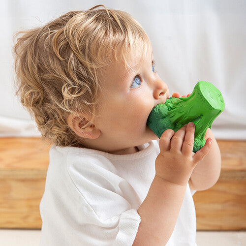 Een baby met blond haar bijt op het groene broccoli bijtspeelgoed.