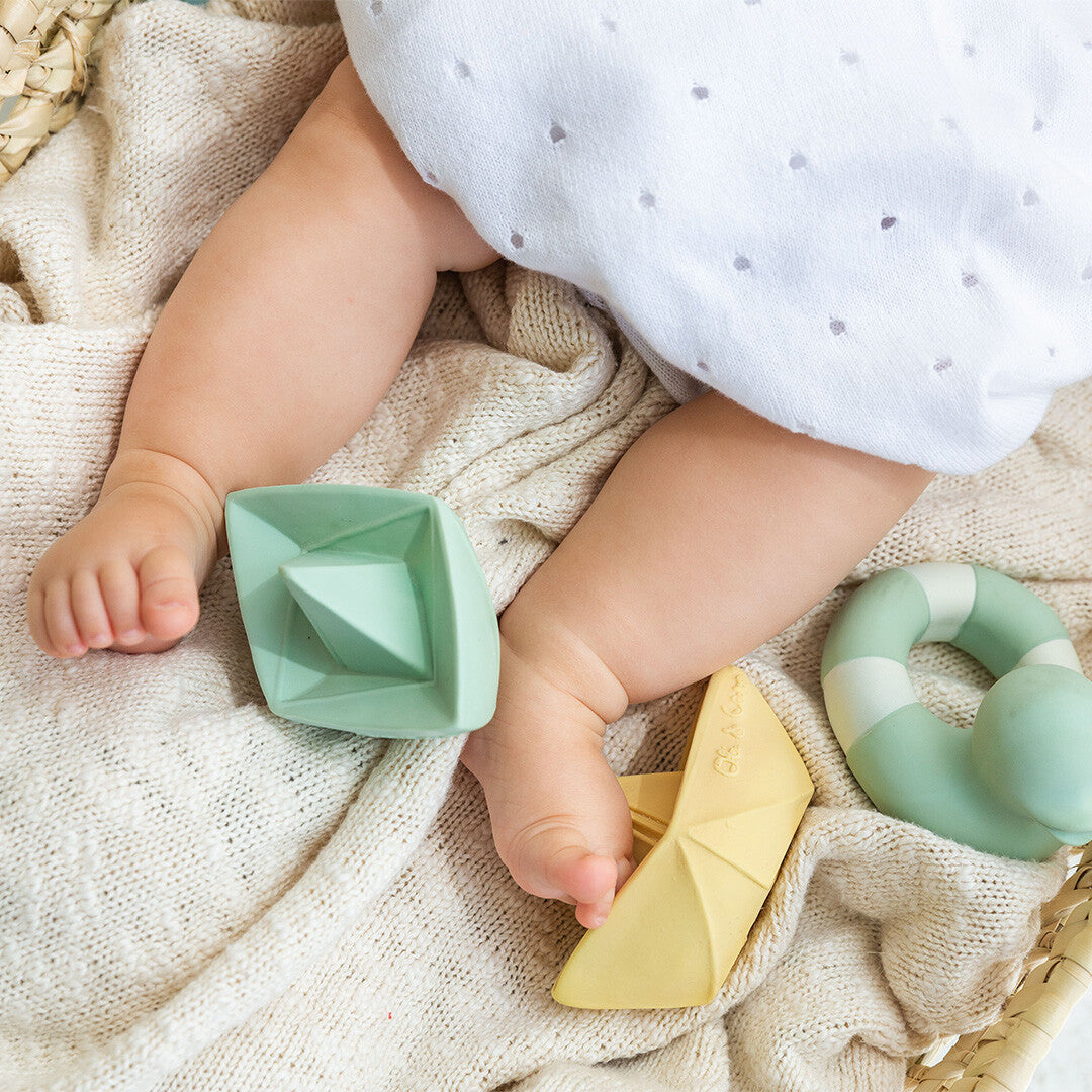 Babybeentjes liggen tussen Oli & Carol bijt- en badspeelgoed in de vorm van twee origami bootjes en een bijtring.
