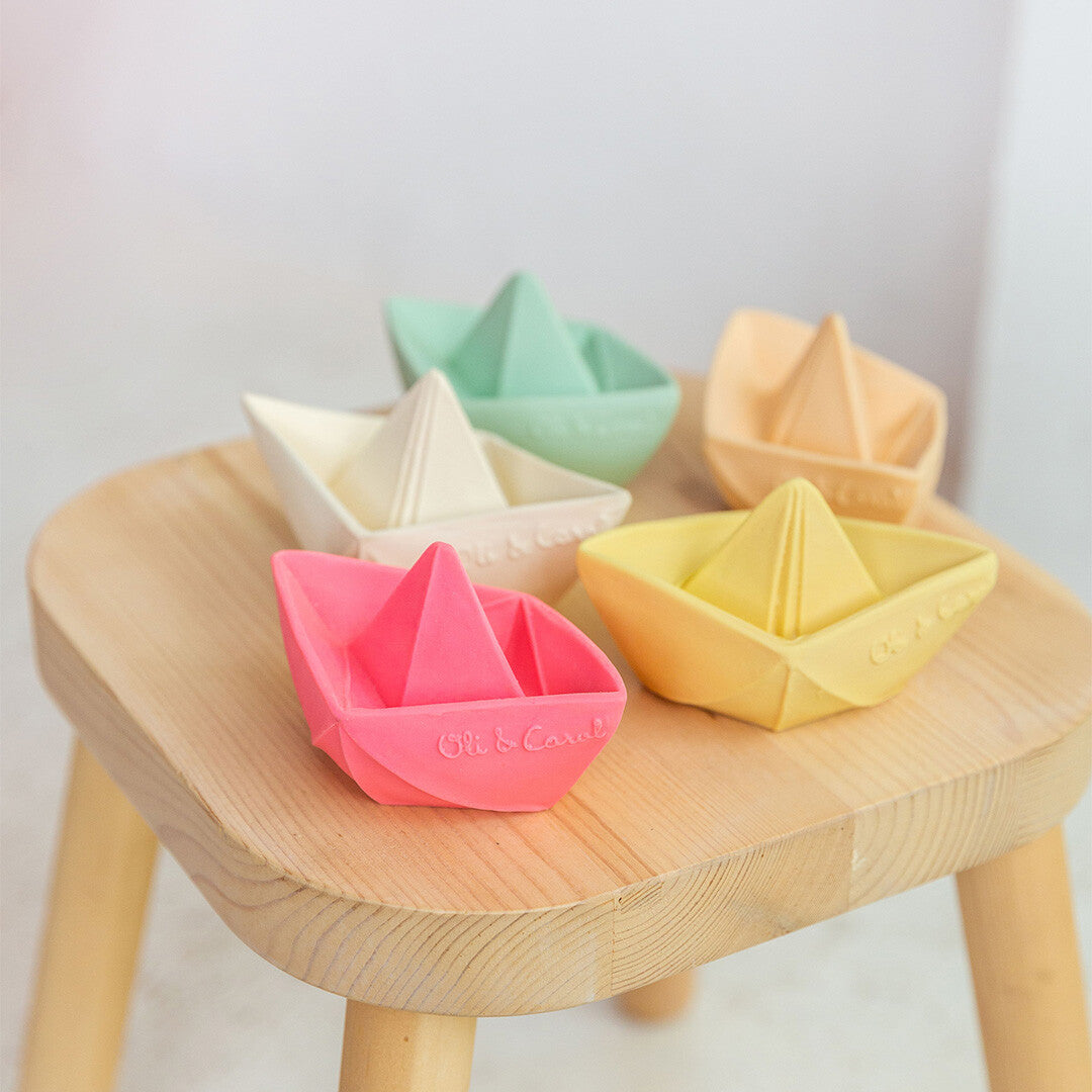 Vijf Oli & Carol bijt- en badspeelgoed origami bootjes in verschillende kleuren staan op een houten krukje.
