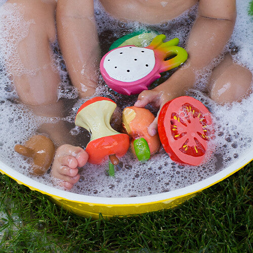 Babyhandjes spelen met het rode tomaten badspeelgoed en andere fruitvormige speeltjes in een schuimend bad.