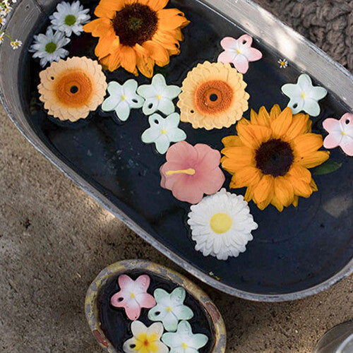 Diverse Oli & Carol babyspeelgoed bijtringen in bloemvorm drijven samen met echte bloemen in een badje water.