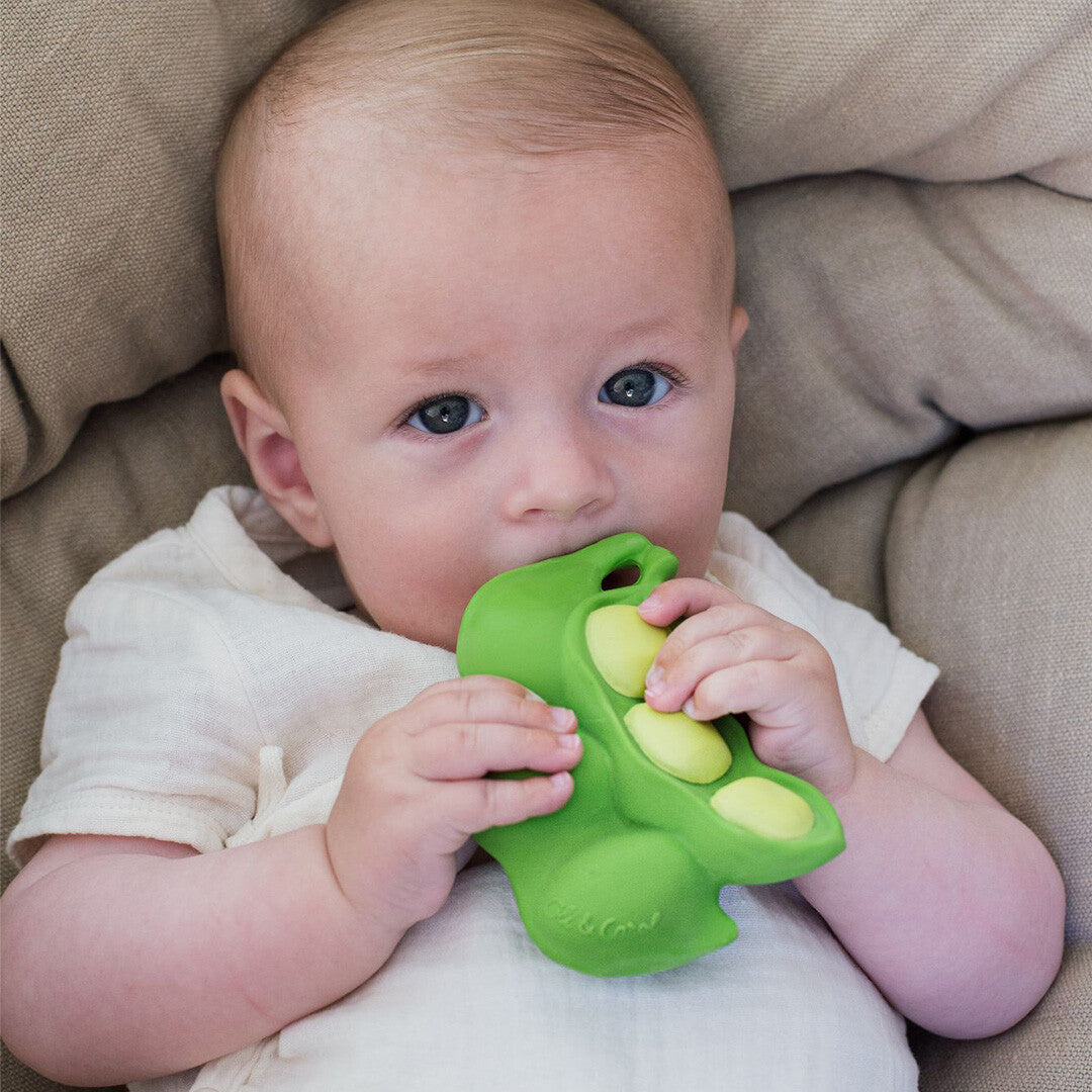 Een baby ligt en houdt het groene edamame bijtspeeltje vast.
