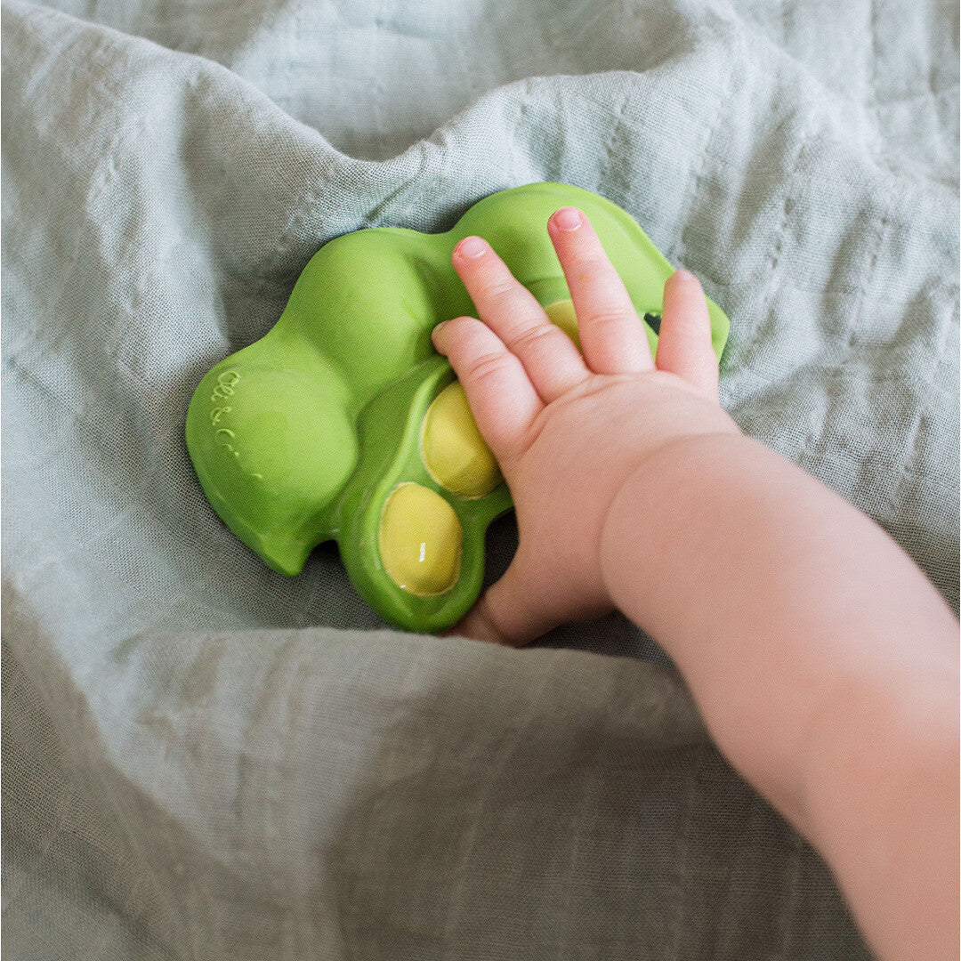 Een babyhandje reikt naar het groene edamame bijtspeeltje op een deken.