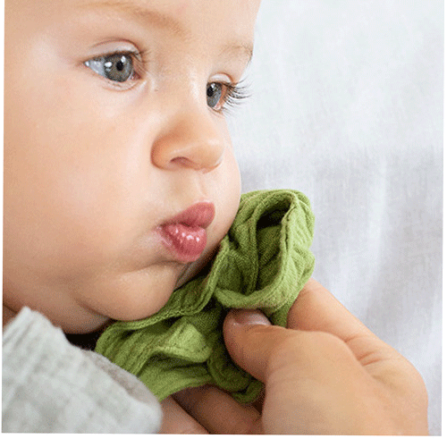 Close-up van een baby die een groen stoffen blad van het babyspeelgoed vasthoudt.