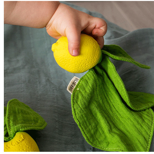 Een babyhandje houdt het gele limoen bijtspeeltje met groene stoffen bladeren vast.
