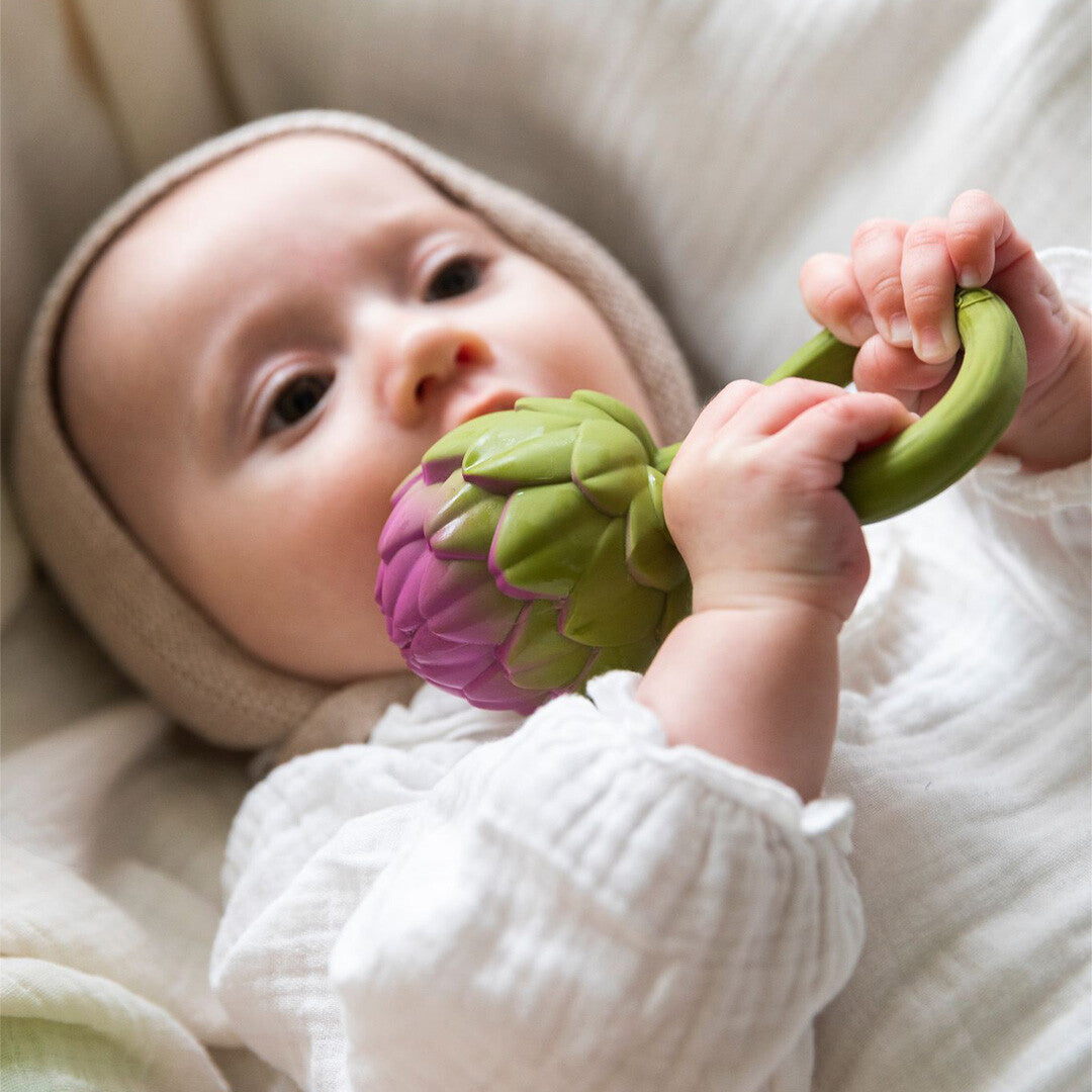 Een baby kauwt op de Oli & Carol artisjok rammelaar.