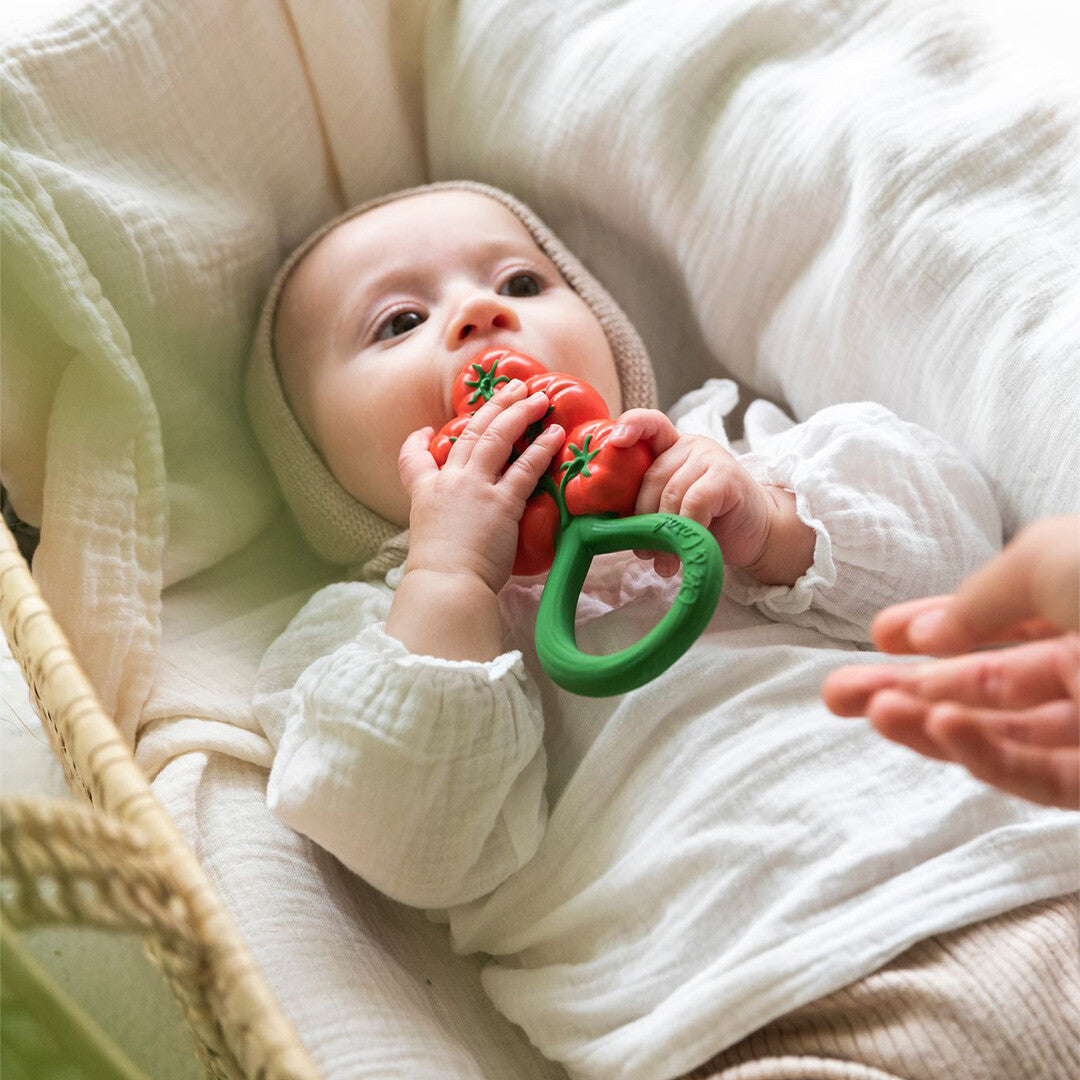 Een baby in een wiegje sabbelt op de Oli & Carol tomaten bijtring.