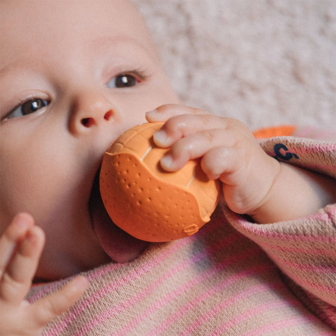 Een baby bijt op een Oli & Carol mandarijn bijtbal.
