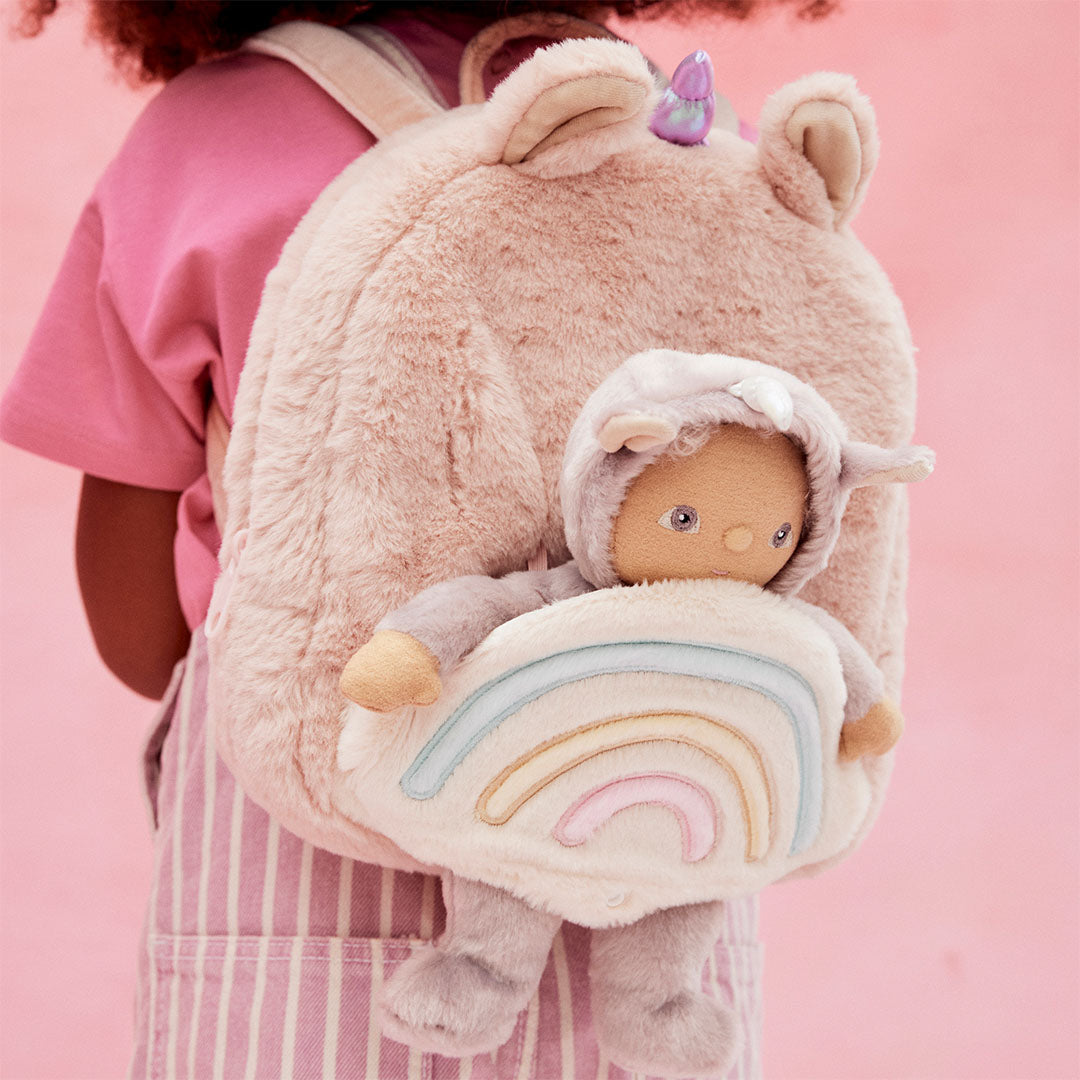 Kind draagt de Olli Ella roze eenhoorn kleuterrugzak met pop in de regenboogzak op de rug.