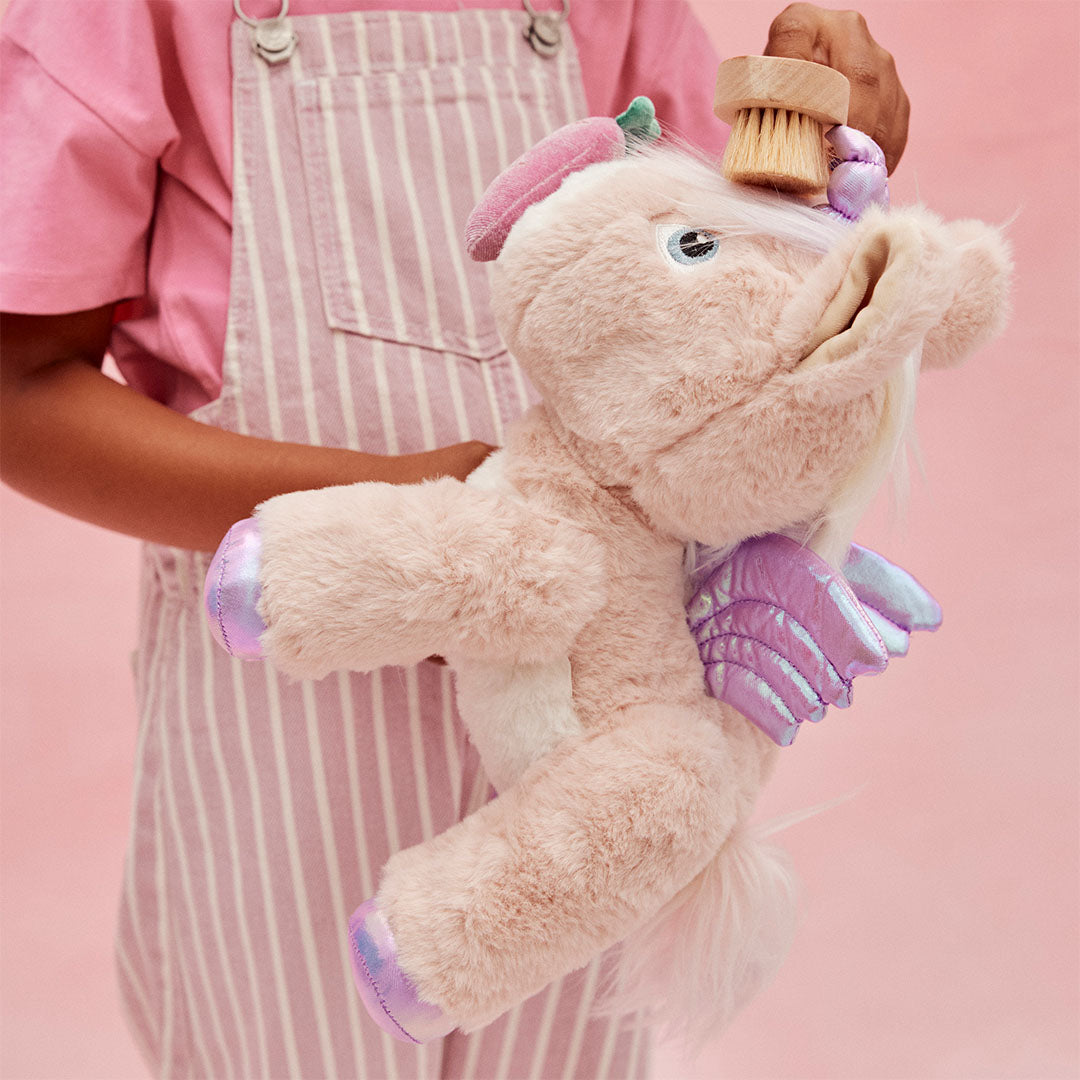 Kinderhanden borstelen de manen van de roze olli ella pluchen eenhoorn knuffel met een houten borstel.