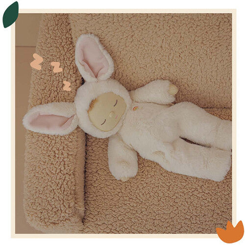 Olli Ella Cozy Dinkum lappenpop in een beige konijnenpakje ligt slapend op een bruine, pluizige deken.