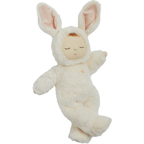 Olli Ella Cozy Dinkum lappenpop in een beige konijnenpakje met een regenboogje op de borst staat met één been opgetrokken.