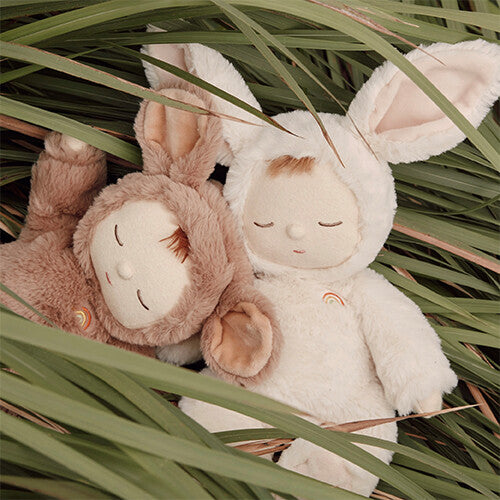 Twee Olli Ella pluchen lappenpoppen, een bruine muis en een witte konijn, liggen in het lange groene gras.