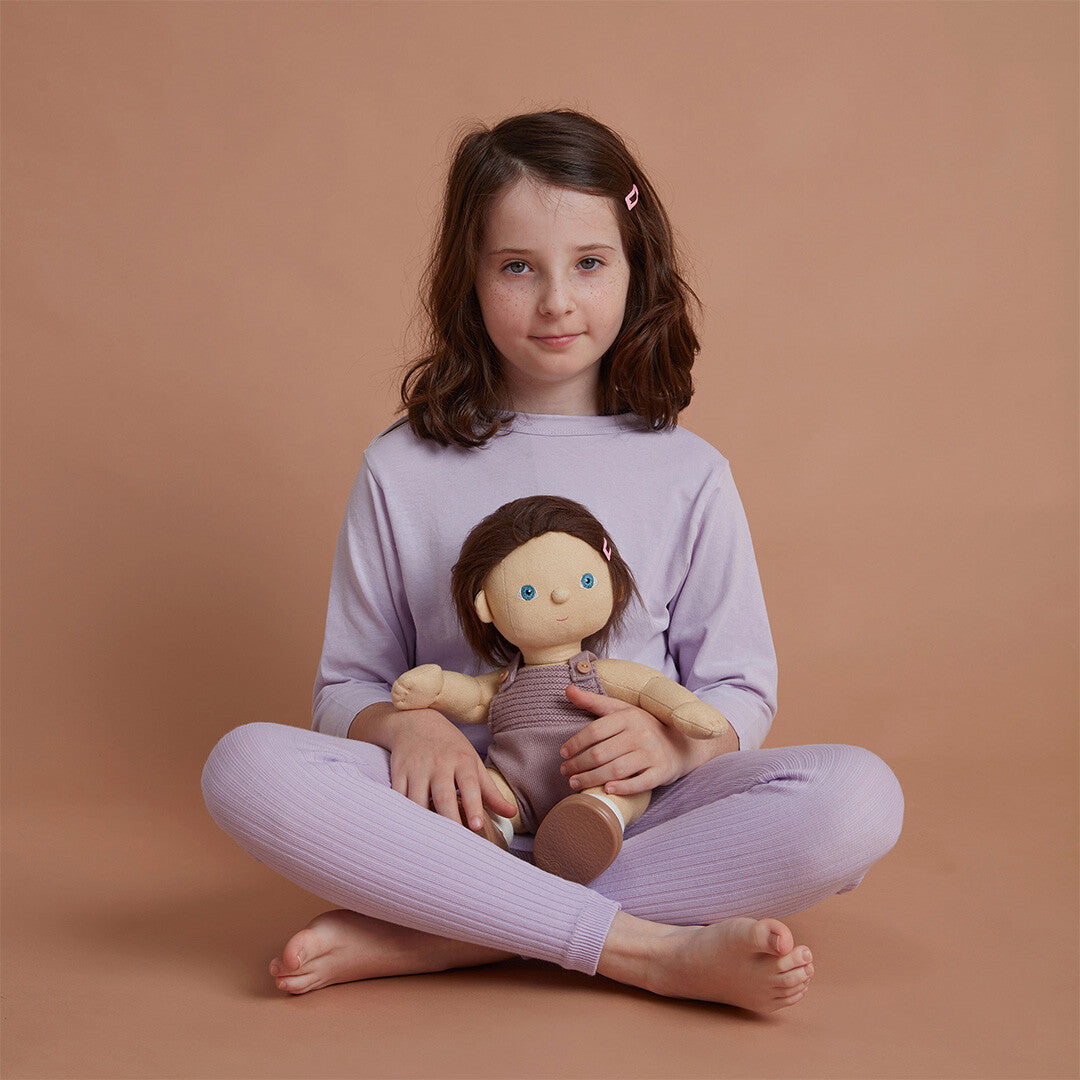 Een kind zit met gekruiste benen en houdt de Olli Ella lappenpop Dinkum Doll Bitsy vast.