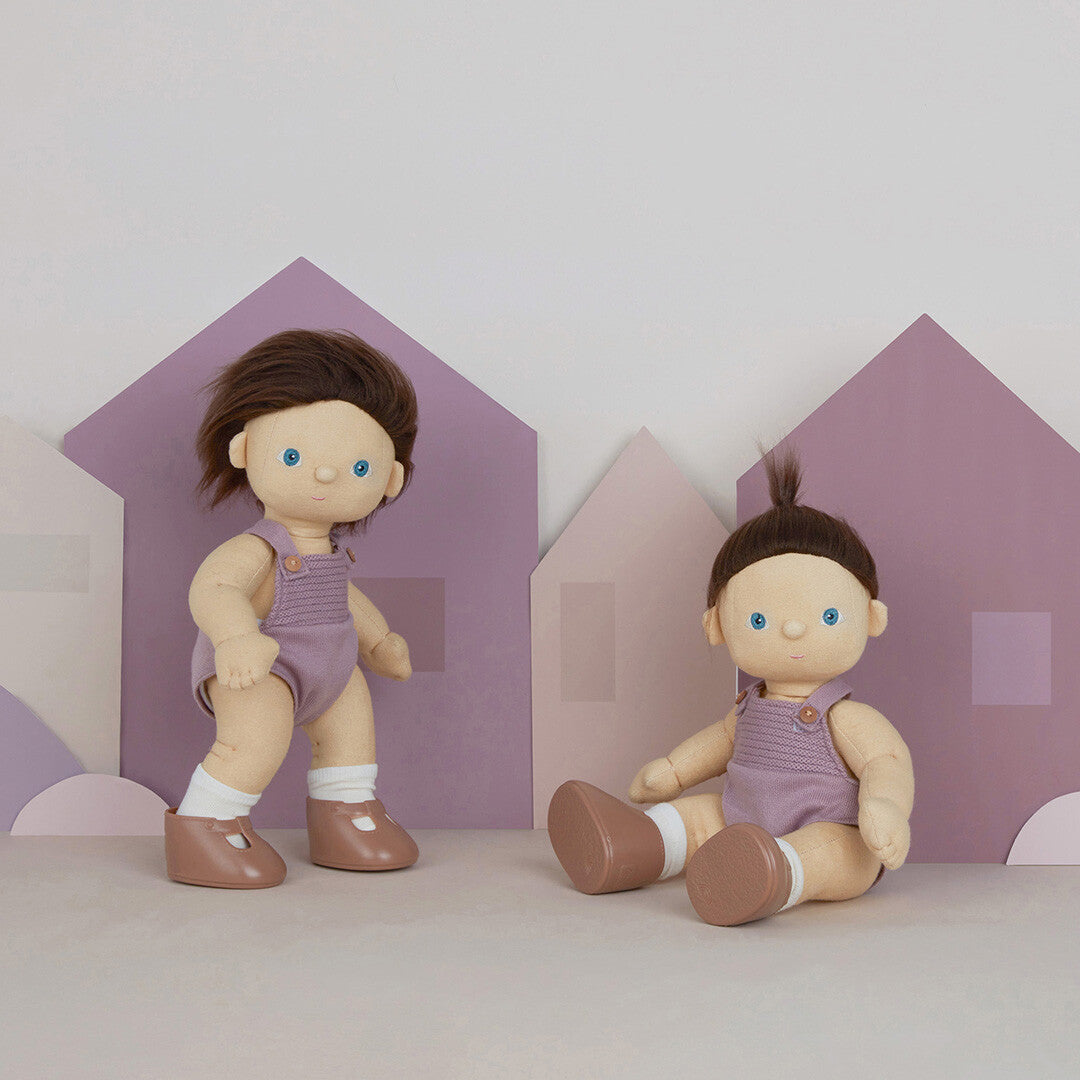 Twee Olli Ella lappenpoppen Dinkum Doll Bitsy, één staand en één zittend, voor paarse huisvormige achtergronden.