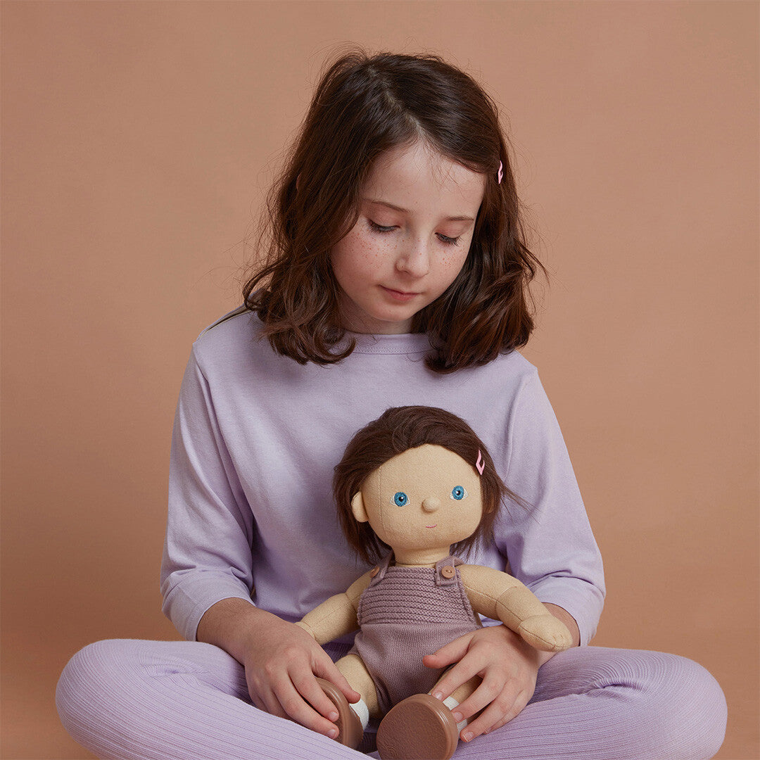 Een kind zit met gekruiste benen en kijkt naar de Olli Ella lappenpop Dinkum Doll Bitsy die ze vasthoudt.