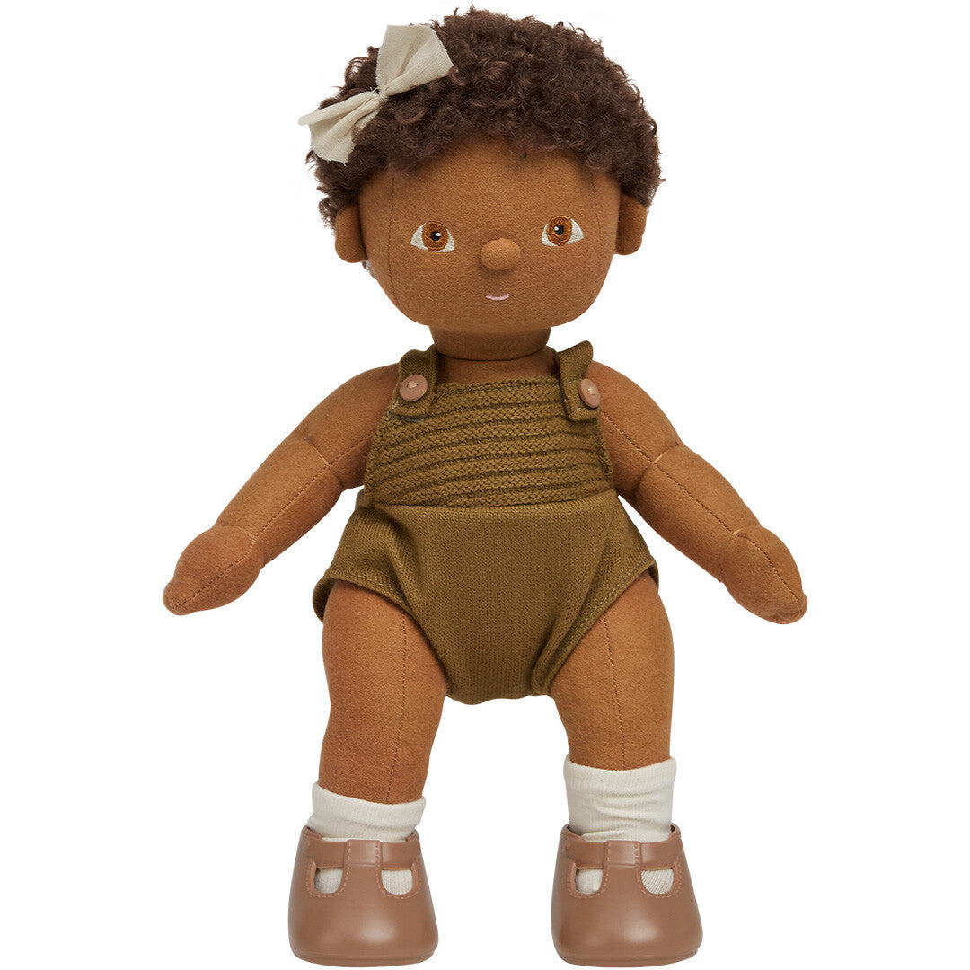 Olli Ella lappenpop Button met bruine huid en krullend haar met strik, staand in een groene gebreide romper en bruine schoenen.