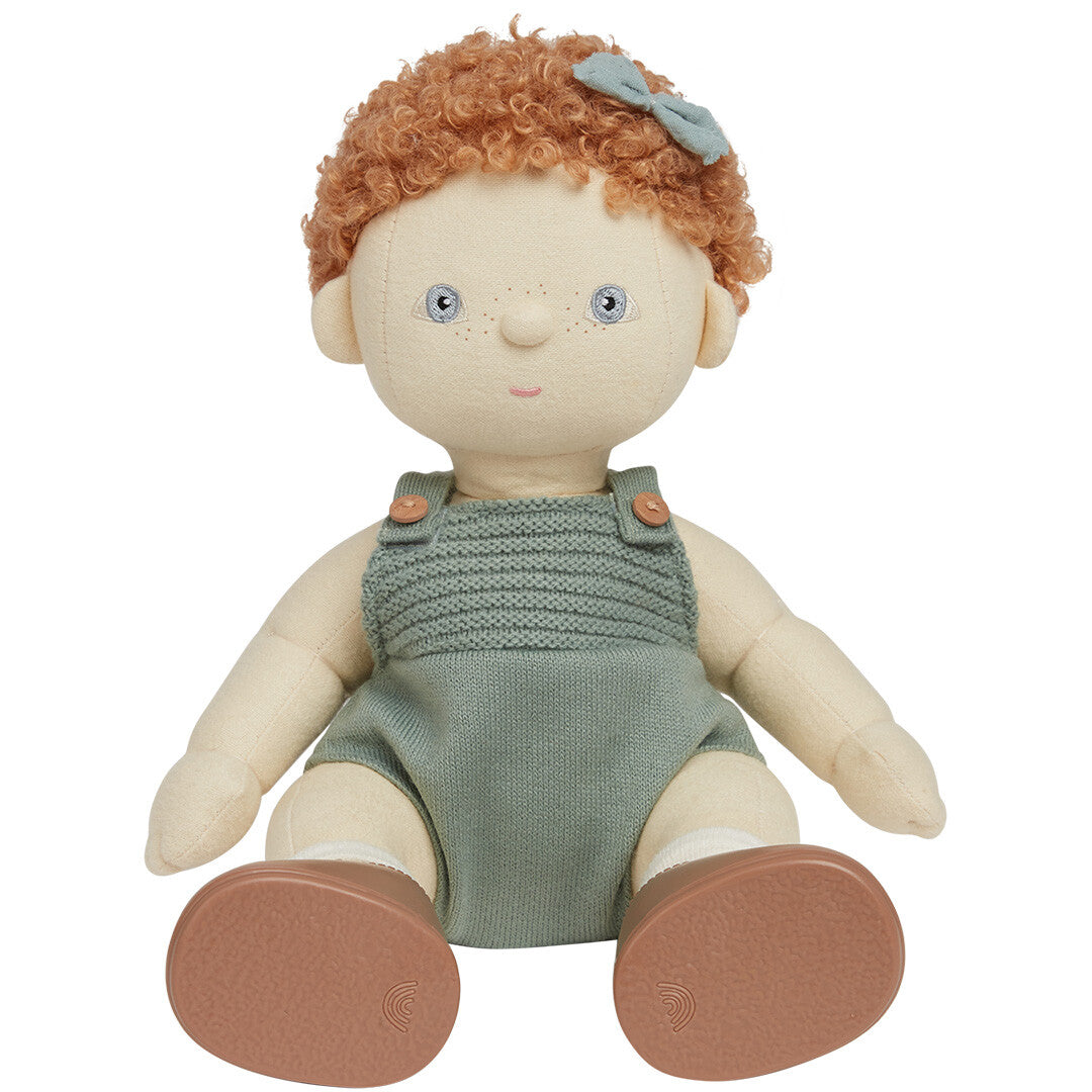 Olli Ella lappenpop Dinkum Doll met rood krullend haar, zittend in een groene gebreide romper en bruine schoenen.