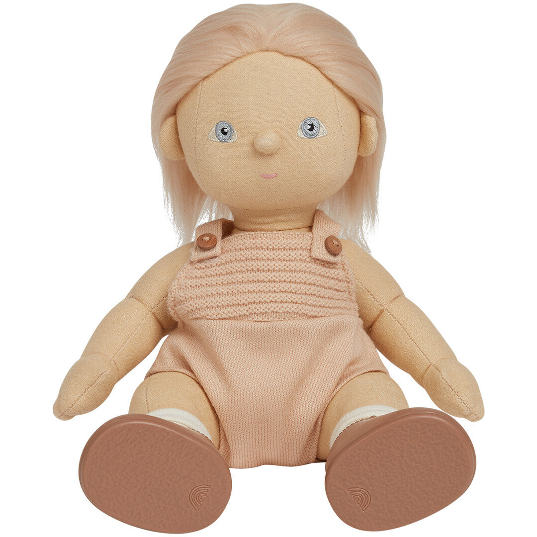 Olli Ella lappenpop met blond haar, zittend in een roze gebreid pakje en bruine schoentjes.