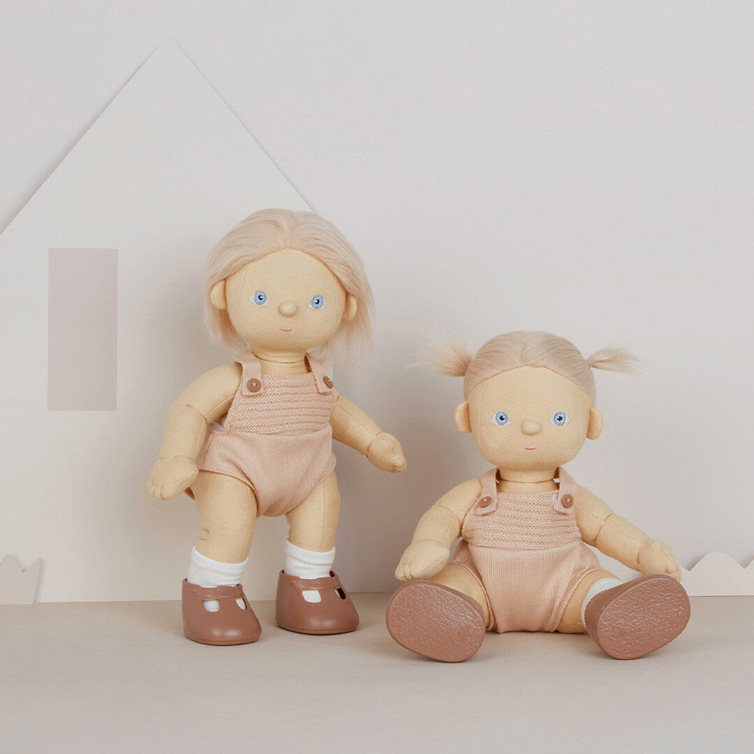 Twee Olli Ella lappenpoppen, één staand en één zittend, in een kamer met een huisvormige achtergrond.