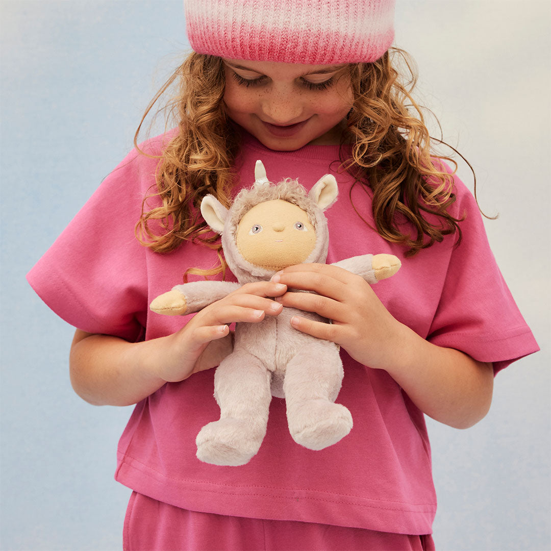 Een kind in een roze outfit houdt de olli ella Uma Unicorn lappenpop vast.