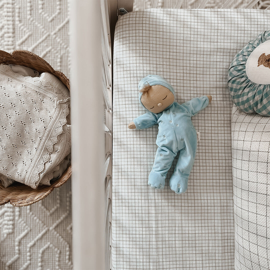Blauwe Olli Ella lappenpop met sterren ligt op een geruit babybedje.