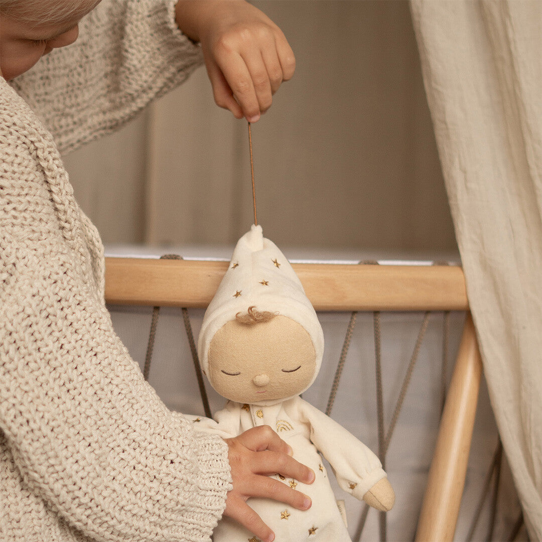 Kinderhanden trekken aan het koordje van een crèmekleurige Olli Ella lappenpop met sterren in een wiegje.