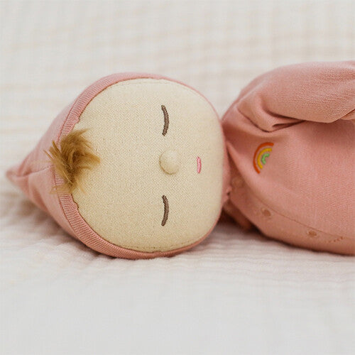 Detail van het hoofd van de roze Olli Ella lappenpop Dozy Dinkum Doll Moppet met gesloten ogen en een regenboogje op de borst.