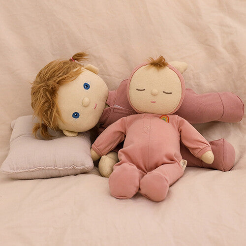 Een roze Olli Ella Dozy Dinkum lappenpop ligt naast een andere pop met open ogen en haar op een bed.