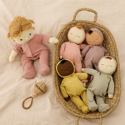 Een Olli Ella pop met open ogen en haar staat naast een mand met vier Dozy Dinkum lappenpoppen in verschillende kleuren.