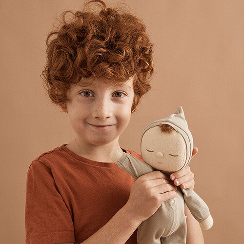 Een jongen met rood krullend haar glimlacht terwijl hij de Olli Ella lappenpop Dozy Dinkum 'pickle' vasthoudt.