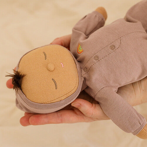 Close-up van de Olli Ella lappenpop Dozy Dinkum Doll Pip in roze onesie met regenboogje, liggend in handen.